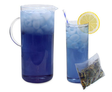 A clear pitcher and glass filled with Flower Power Cold Brew Tea Pods – A Color-Changing Tropical Floral Fantasy 🌺, blue butterfly pea flower iced tea with a lemon slice and striped straw. Caffeine-free, refreshing, with a transparent tea pod beside them.
